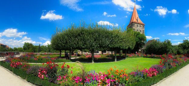 A landscape plan with boxwood borders, colorful flower beds, and a circular garden bed shaded by trees.