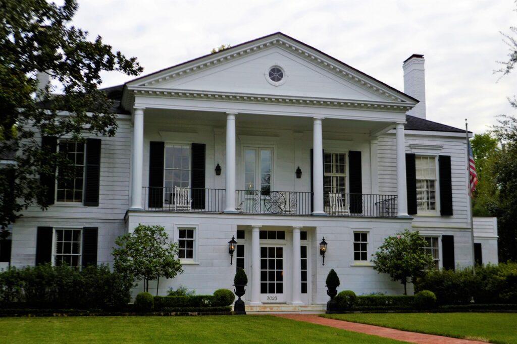 A large lawn, topiaries, and small trees highlight the entry of this home.