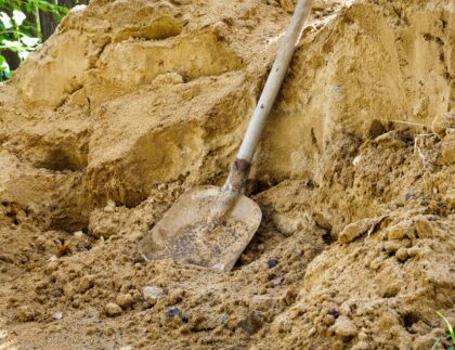 A flat shovel, an essential tool for moving landscaping dirt, beside a pile of sand.