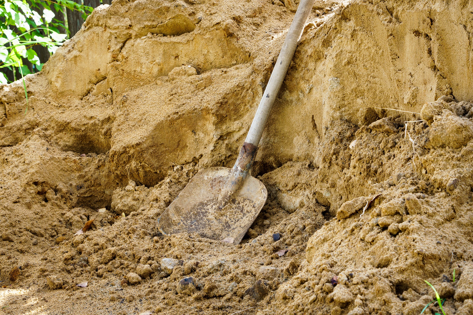A flat shovel, an essential tool for moving landscaping dirt, beside a pile of sand.