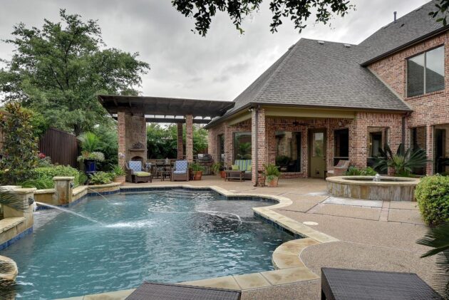 This backyard pool landscaping utilizes an irregular pool shape with a custom tile deck to craft an upscale look.